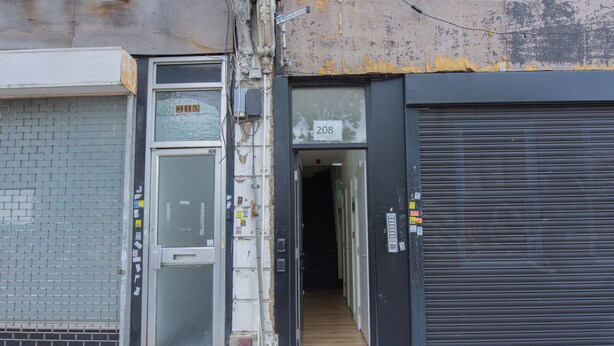 En stängd butik med en metallrulljalusi och ett tydligt synligt dörrnummer, 208.