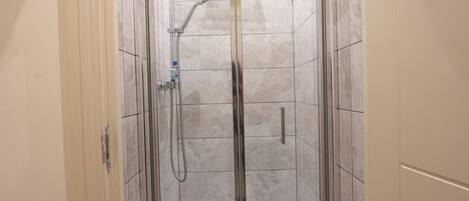 A walk-in shower with a glass door, tiled walls, and a handheld showerhead.