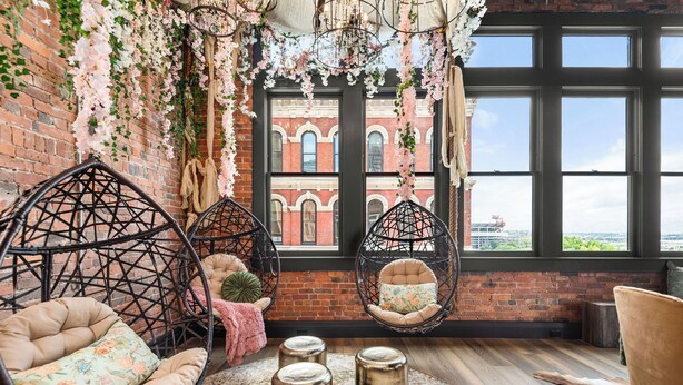Una habitación acogedora con sillas colgantes, un ventanal con vistas y detalles decorativos como flores y una lámpara de araña.