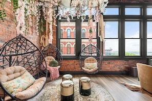Um quarto acolhedor com cadeiras suspensas, uma janela ampla com vista e detalhes decorativos como flores e um lustre.