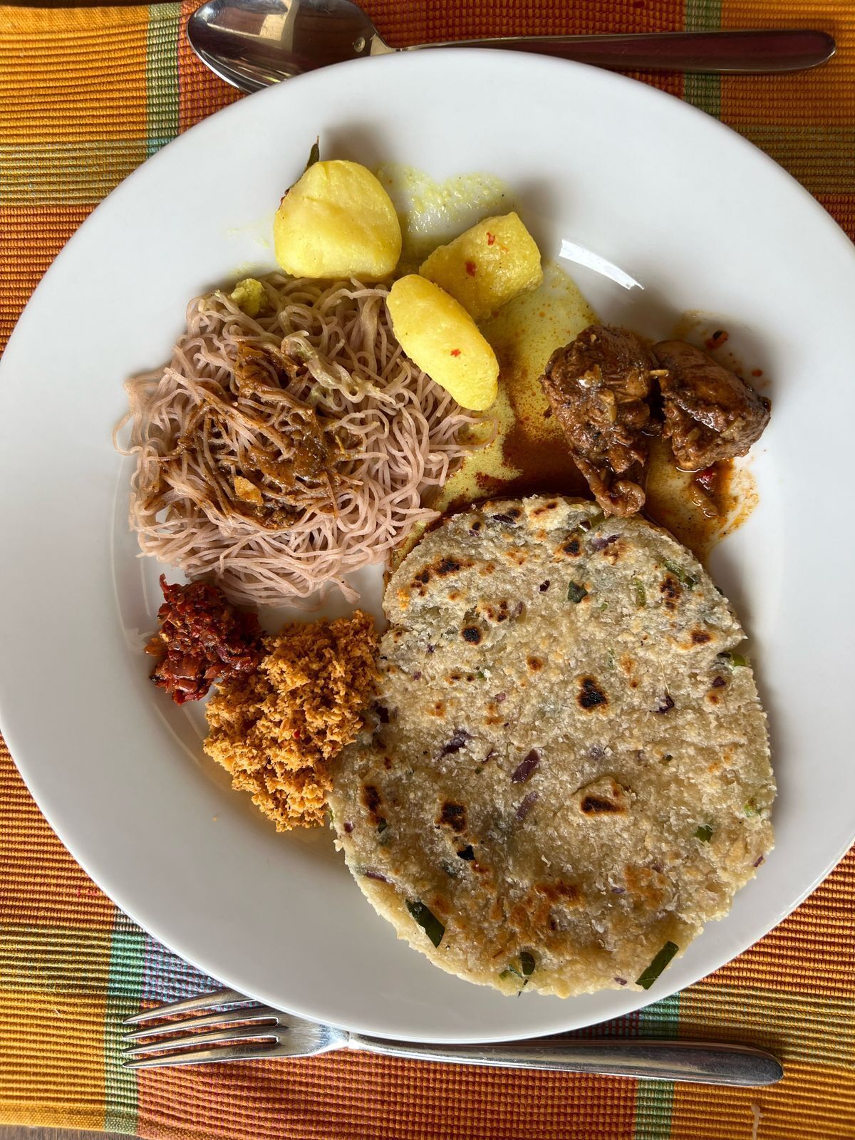 A plate of food with noodles, potatoes, meat, and a flatbread.
