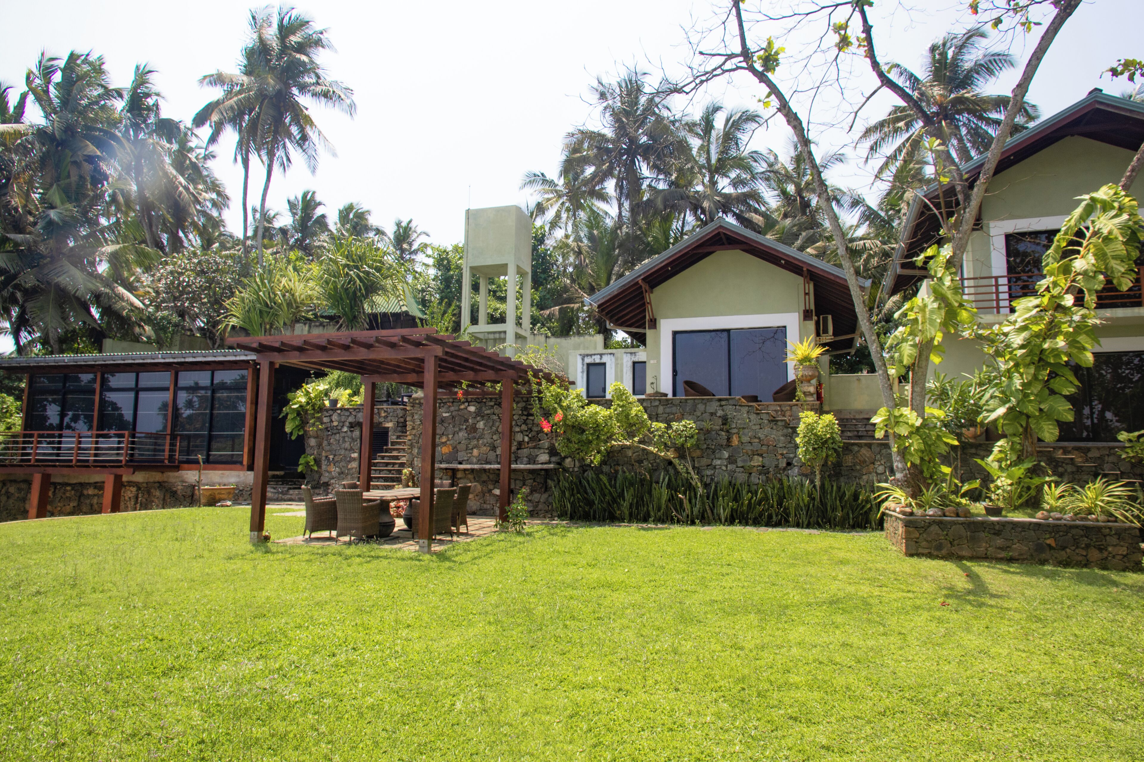 A house with a stone wall, a wooden pergola, and a lawn.