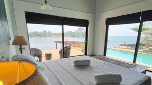 Een slaapkamer met een groot bed, een lamp en uitzicht op zee door een schuifdeur.