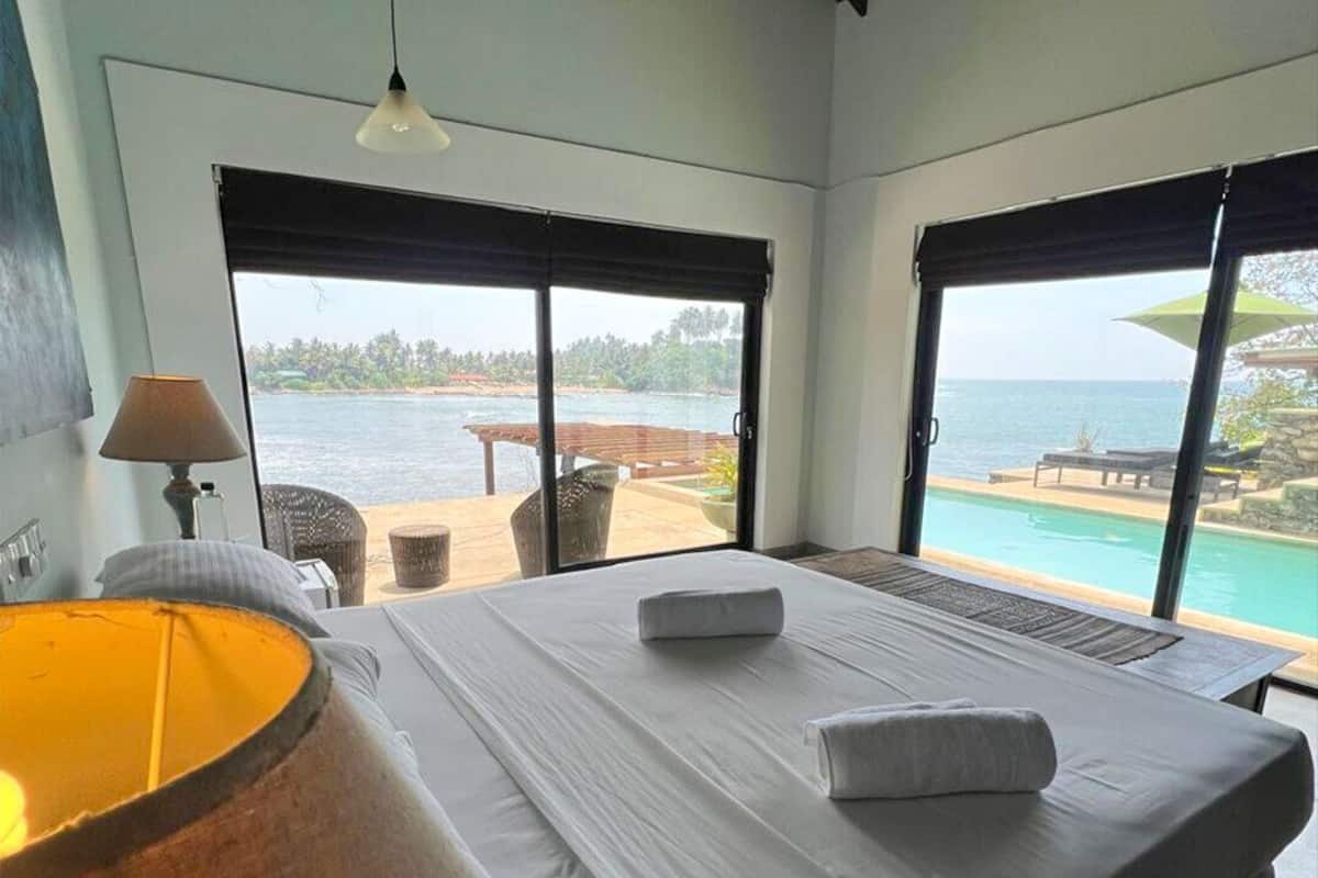 Een slaapkamer met een groot bed, een lamp en uitzicht op zee door een schuifdeur.