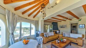 A spacious living area with a high ceiling, wooden beams, a large sofa, a dining table with oranges, and a view of the city. - Casa Palmeras - Moraira (Moraira)