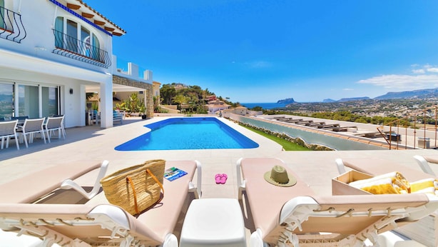A pool area with lounge chairs, a view of the sea, and a building with a balcony. - Casa Palmeras - Moraira (Moraira)