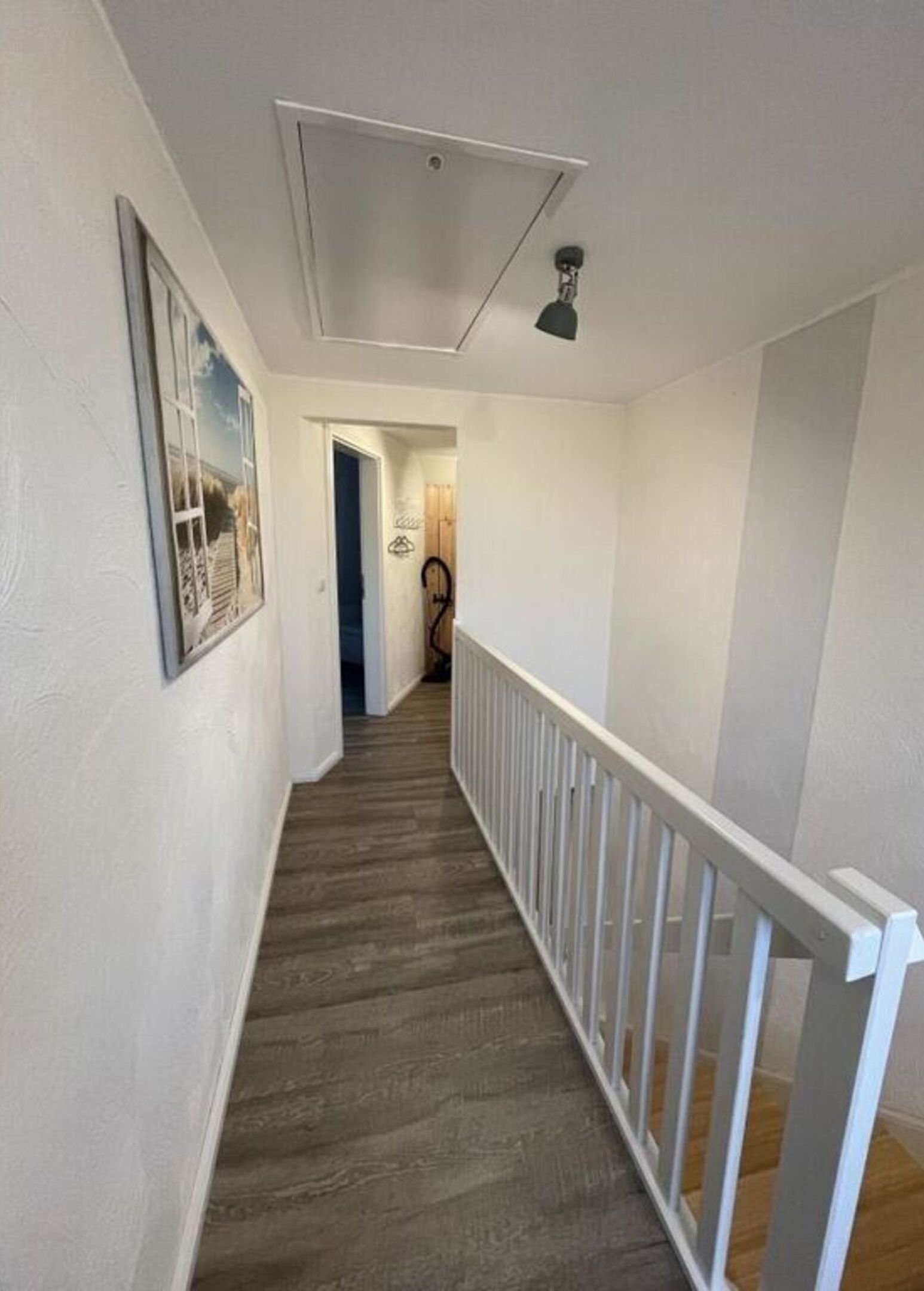 A narrow hallway with a white railing, wooden flooring, and a ceiling light fixture.