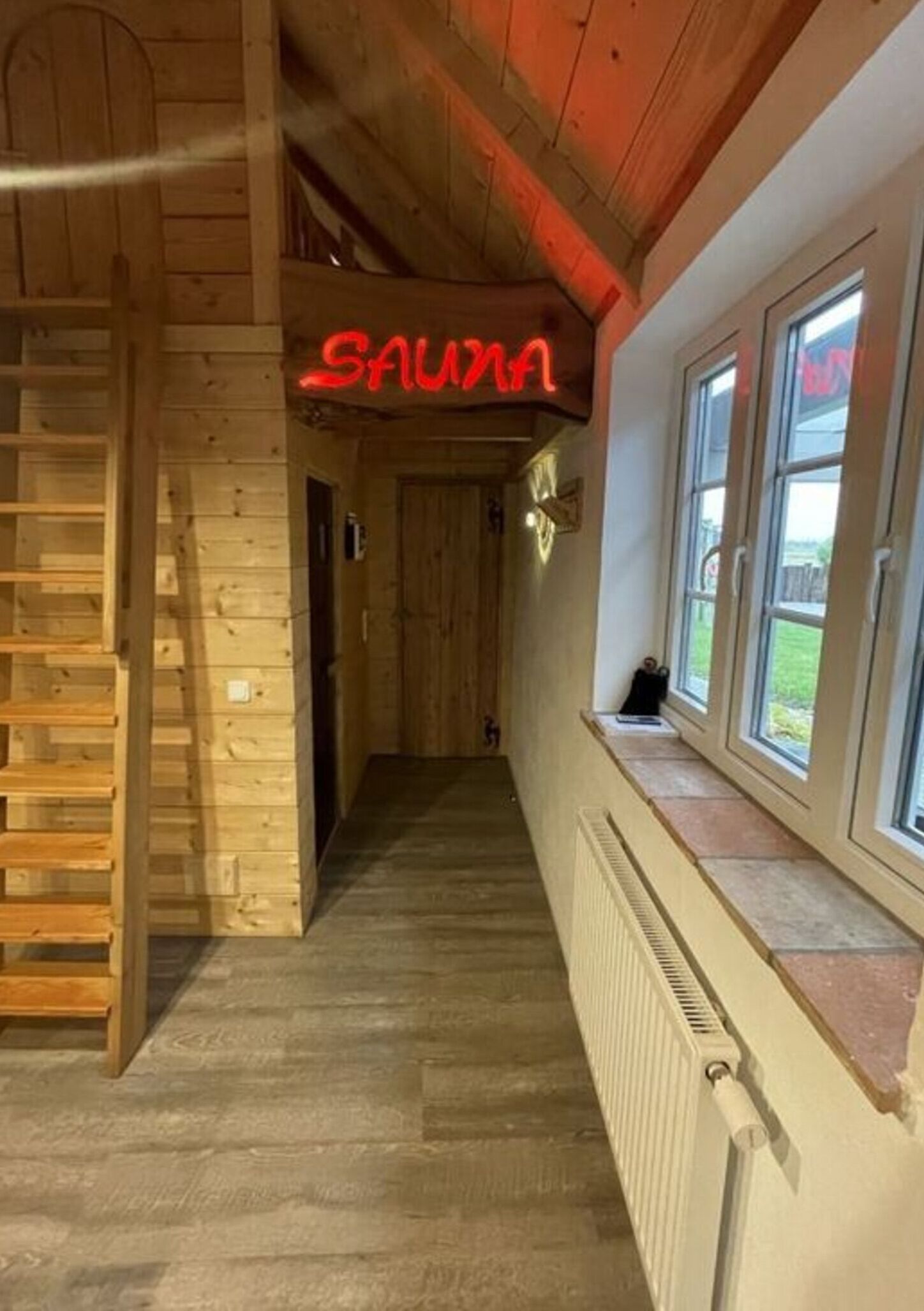 Um corredor de madeira com um letreiro de neon que diz "SAUHA" e uma janela com vista para o exterior.