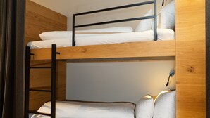 Un letto a castello con testiera in legno e struttura in metallo nero, biancheria da letto bianca e una lampada da comodino.
