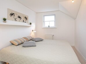A bedroom with a bed, pillows, a wall-mounted shelf with plants, a window, and a radiator. - 8 Person Holiday Park Home in Bogense (Bogense)