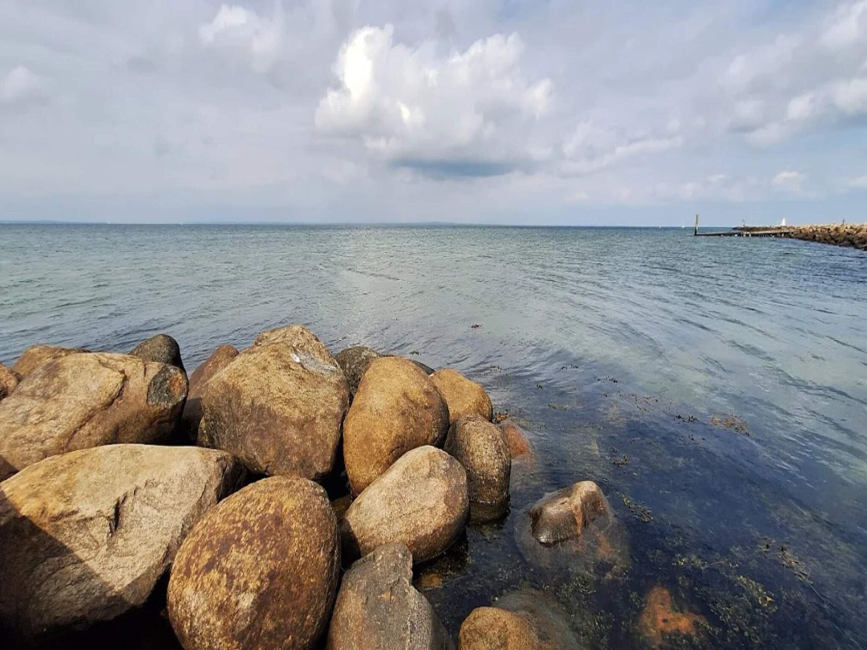 A rocky shoreline with clear water and a distant pier.