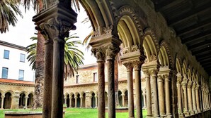 A courtyard with stone columns and arches, a building in the background, and a palm tree. - Apartment in Ourense Near Thermal Baths (Ourense)