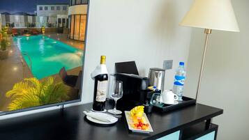 A hotel room with a pool view, a minibar, a lamp, and a dining setup with fruit.