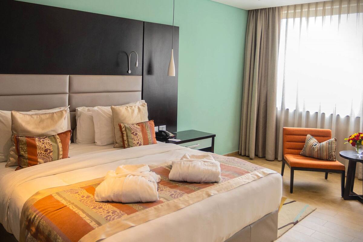 Una camera d'albergo con un letto grande, un comodino, una sedia e una finestra con tende.