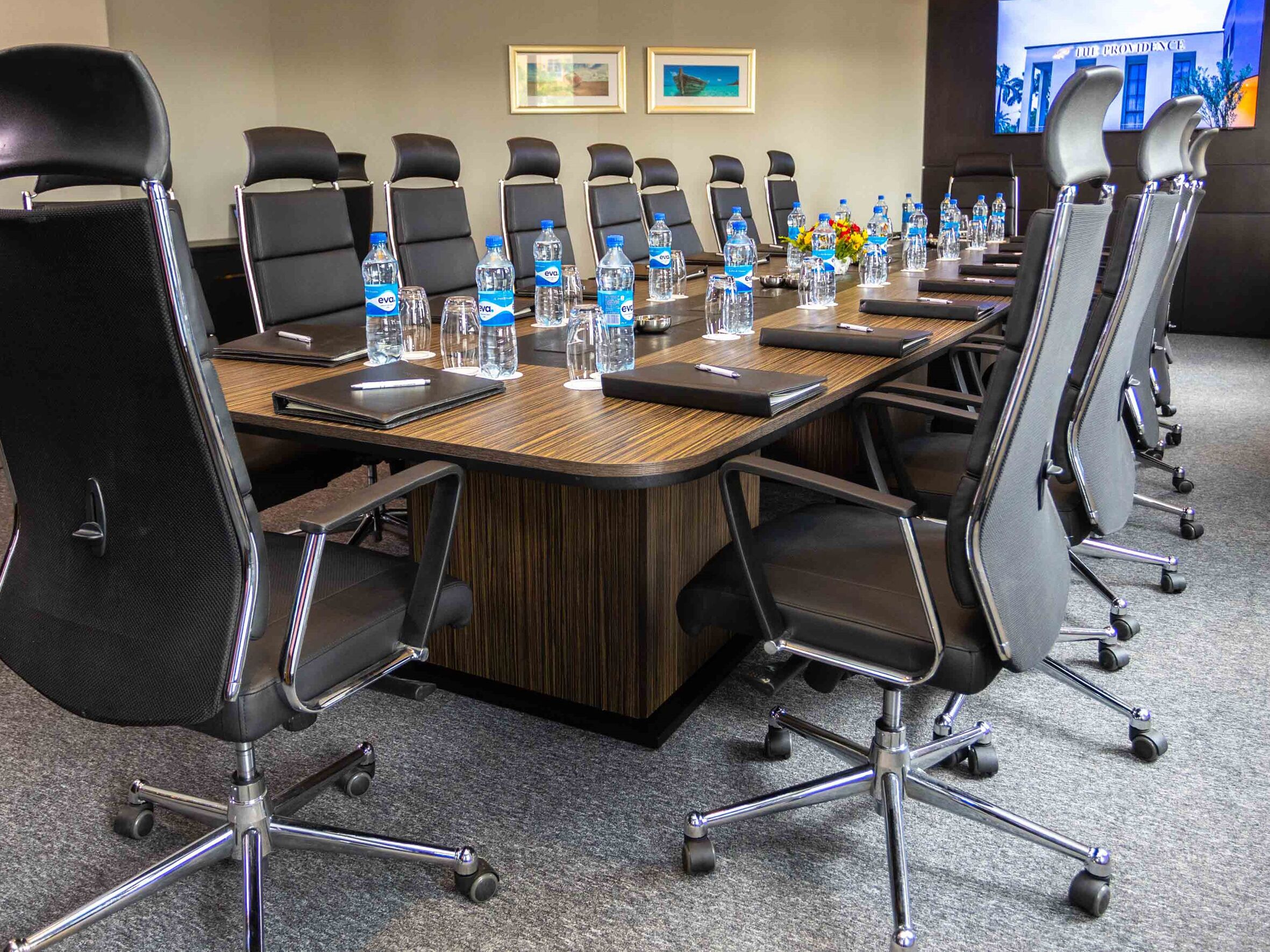 A conference room with a long table, black chairs, water bottles, and a TV screen displaying 'THE PROVIDENCE'.