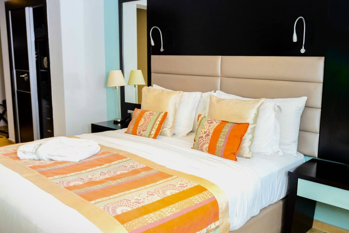 Un letto rifatto con una coperta a righe, una testiera con due luci fissate al muro e un comodino con una lampada.
