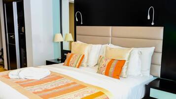 A neatly made bed with a striped blanket, a headboard with two wall-mounted lights, and a nightstand with a lamp.