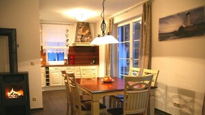 A cozy dining area with a wooden table and chairs, a fireplace, and a window with curtains. - Holiday Home Hannah Comfortable Vacation Home (Koserow)