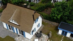 A two-story house with a stone patio, a small outdoor seating area, and a separate building with a blue roof. - Holiday Home Hannah Comfortable Vacation Home (Koserow)
