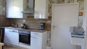 A compact kitchen with white cabinets, a built-in oven, a coffee maker, and a small refrigerator. - Csilla Comfortable Holiday Residence (Kaltennordheim)