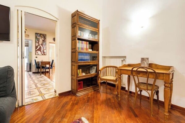 Una habitación con piso de madera, una estantería, una mesa de comedor con sillas y un televisor en la pared.