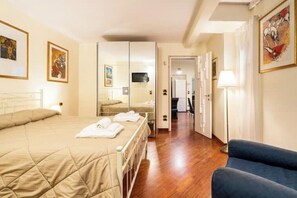 Habitación de hotel con cama, una silla, un espejo y obras de arte en las paredes.