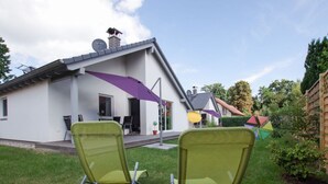 Une maison dotée d’un patio comprenant deux chaises de jardin vertes et un parasol violet.