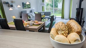 Un coin repas avec une table mise pour le petit-déjeuner, un panier de pain et une vue sur l’extérieur.
