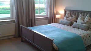 Une chambre à coucher avec un lit, une fenêtre avec des rideaux, une lampe de chevet et une vue sur la verdure à l’extérieur.