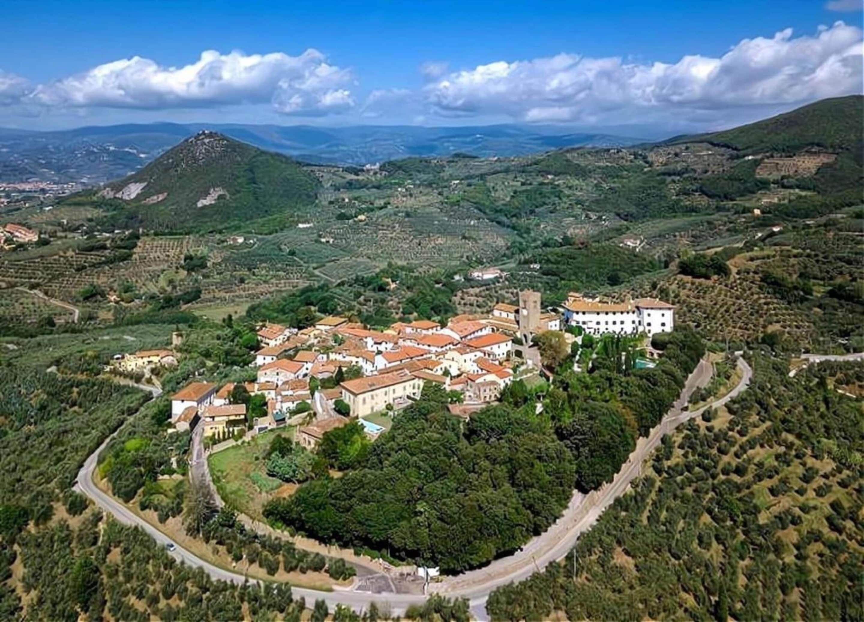 A town with a central square, surrounded by buildings with red-tiled roofs, and a prominent tower.