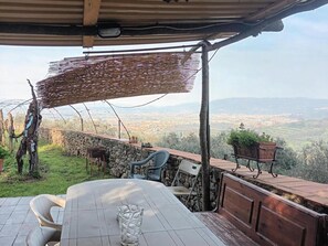 A covered outdoor seating area with a stone wall, a table, chairs, and a view of a cityscape. - Luxury Retreat in Montevettolini (Monsummano Terme)