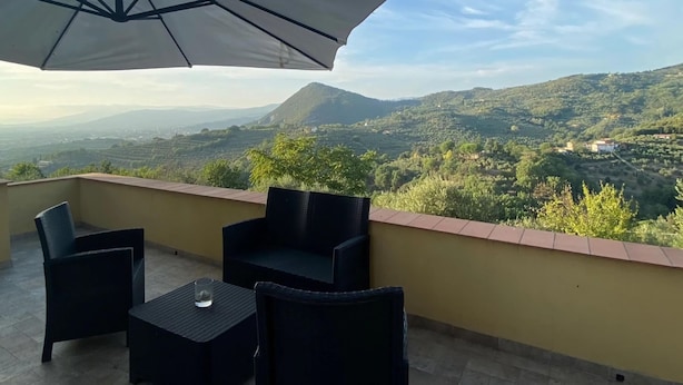 Un balcón con mesa y sillas, un parasol grande y vistas panorámicas de un paisaje montañoso.
