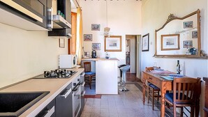 Cocina compacta con estufa a gas, microondas y pileta. Hay un comedor con una mesa y sillas de madera.