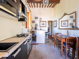Cocina compacta con estufa a gas, microondas y pileta. Hay un comedor con una mesa y sillas de madera.