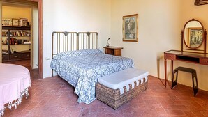 Un dormitorio con cama, mesita de noche, cómoda, silla, estantería y puerta que da a otra habitación.