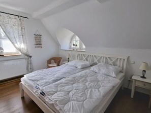 Un dormitorio con una cama grande, una mesita de noche pequeña, una silla, una ventana con cortinas y un espejo.