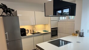 Et moderne køkken med hvide skabe, et rustfrit stål køleskab, indbygget ovn og en stor ø med vask.
