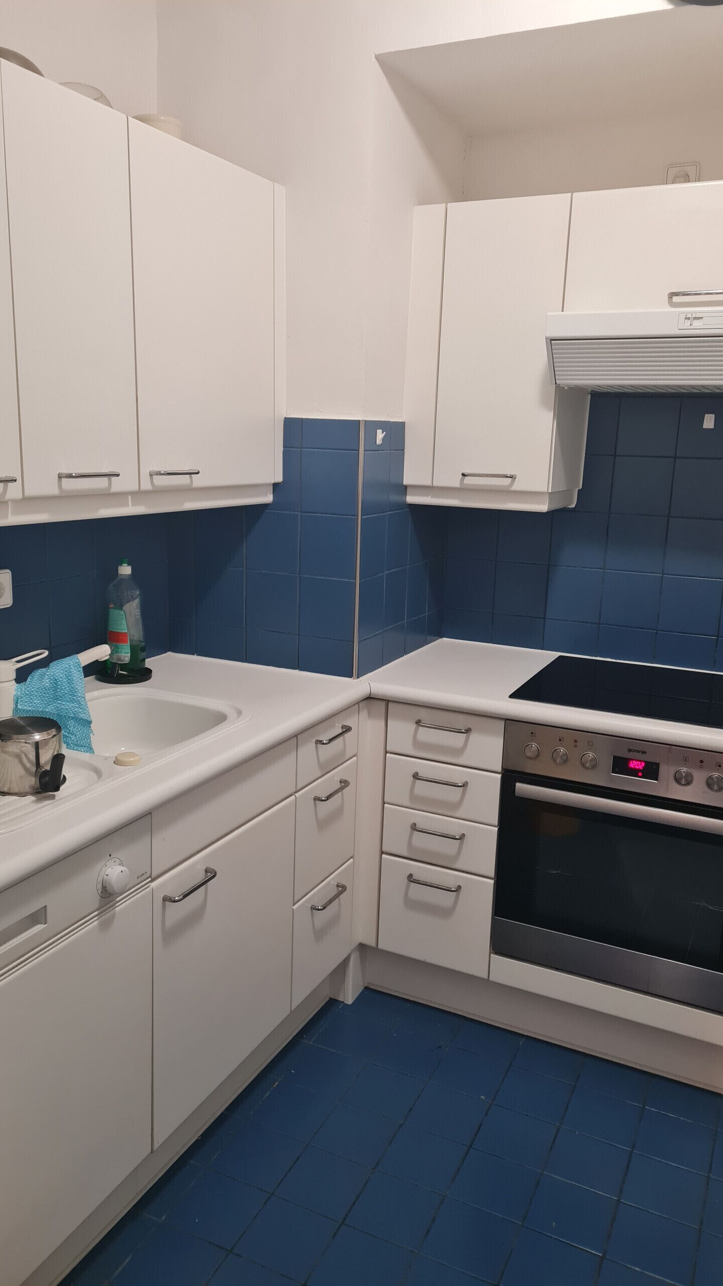 A kitchen with white cabinets, a blue-tiled backsplash, a sink, a stove, and a clock displaying 12:09.