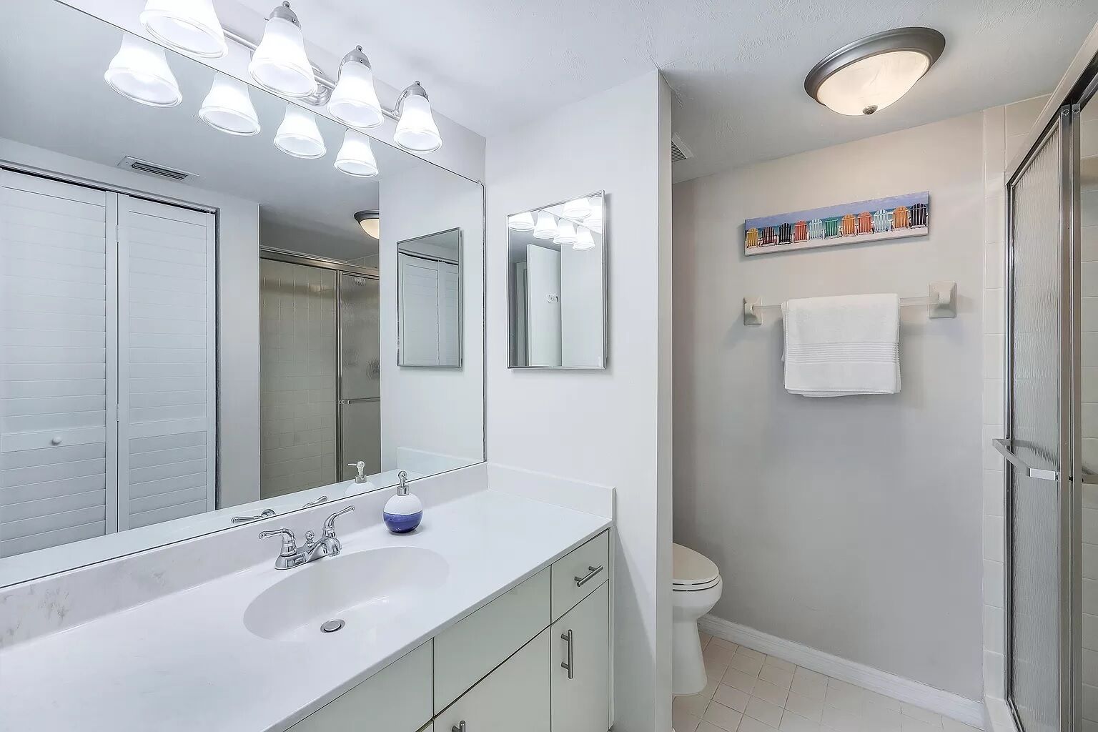 A modern bathroom with a large mirror, white vanity, and a shower area.