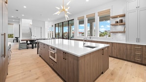 Une cuisine moderne dotée d’un grand îlot central, de meubles en bois et d’un lustre original.