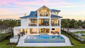 Une maison à deux étages dotée d’une piscine, d’un espace salon extérieur et d’une terrasse couverte.