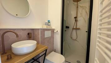 A bathroom with a round sink, a toilet, and a glass-enclosed shower.