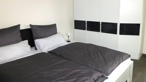 A bedroom with a bed, two pillows, a bedside table with a lamp, and a white wardrobe with black panels.
