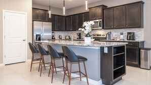 A modern kitchen with dark cabinets, stainless steel appliances, and a central island with bar stools.