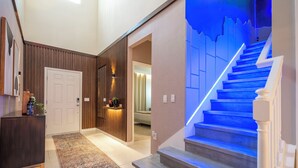 A modern interior with a wooden panel wall, a reception desk, a staircase with blue lighting, and a patterned rug.