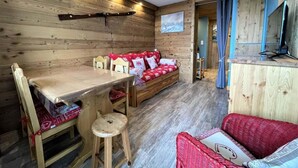 Ein gemütliches Zimmer mit einer Holzwand, einem Sofa mit roten Kissen, einem Esstisch und einem Stuhl.