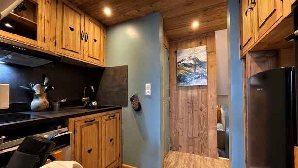 Eine kompakte Küche mit Holzschränken, einer schwarzen Arbeitsplatte und einem Edelstahlkühlschrank.