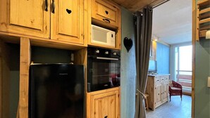 Eine kompakte Küche mit Holzausstattung, einem schwarzen Kühlschrank, einer Mikrowelle und einem Backofen.