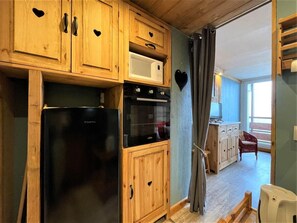 A compact kitchen with wooden cabinets, a black refrigerator, a microwave, and an oven.