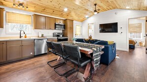 A modern kitchen with wooden ceiling, stainless steel appliances, and a dining area with a table and chairs.